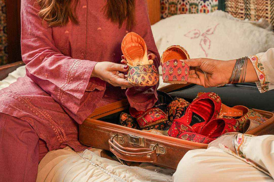 Women holding embroidered khussa shoes from a suitcase, traditional Pakistani footwear