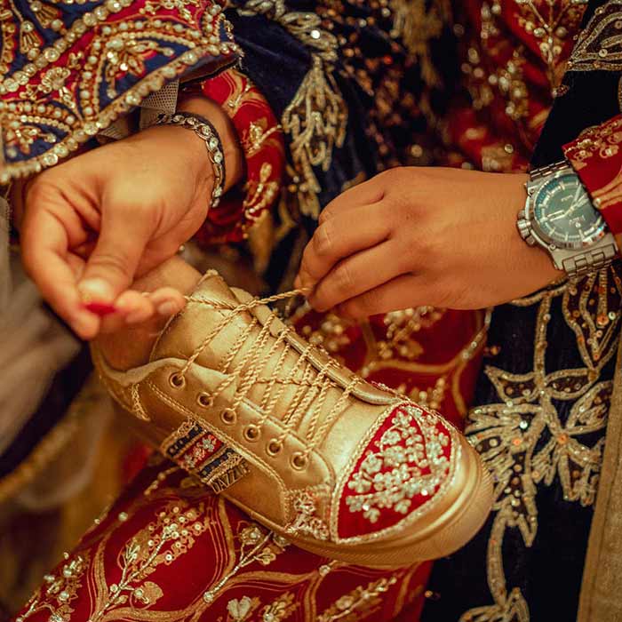Woman tying gold embroidered sneaker with traditional Pakistani bridal dress