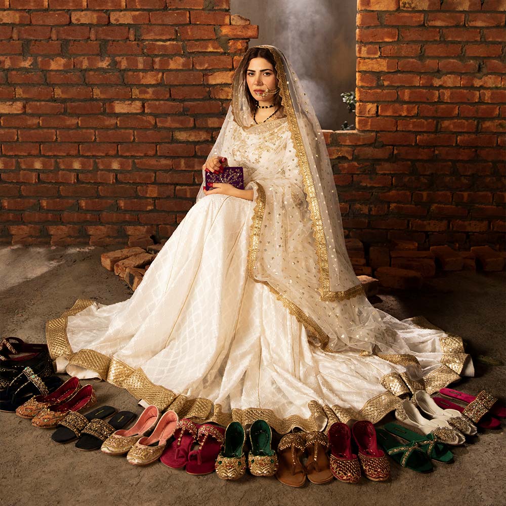 Woman in white traditional dress surrounded by colorful khussa shoes and kolhapuri sandals